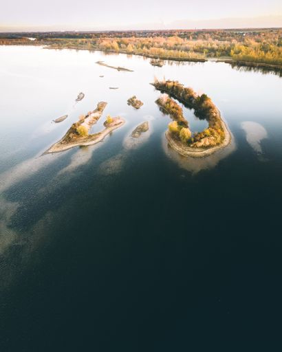 An aerial shot of small islands with trees near the coast covered in forests during the fall