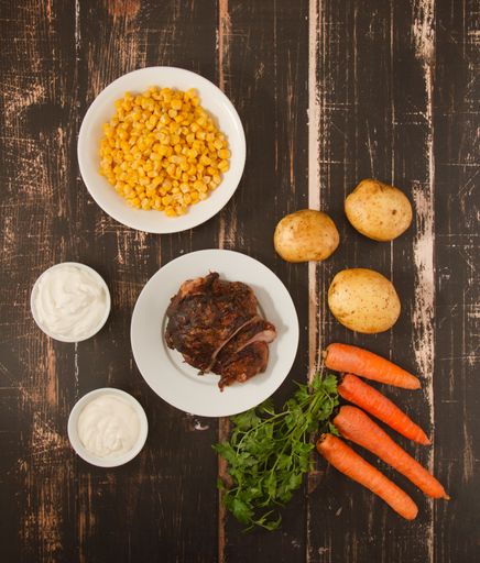 A vertical top view of wooden table with roast beef and ingredients for a salad