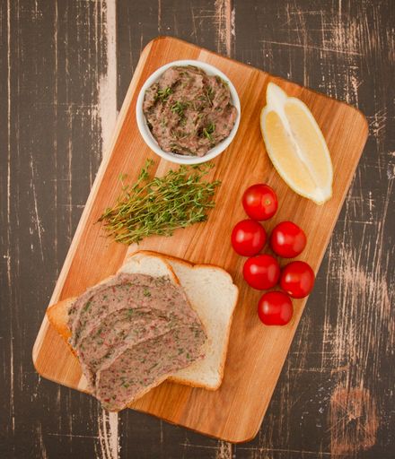 A top view of a wooden board with slices of bread, a spread, and tomatoes