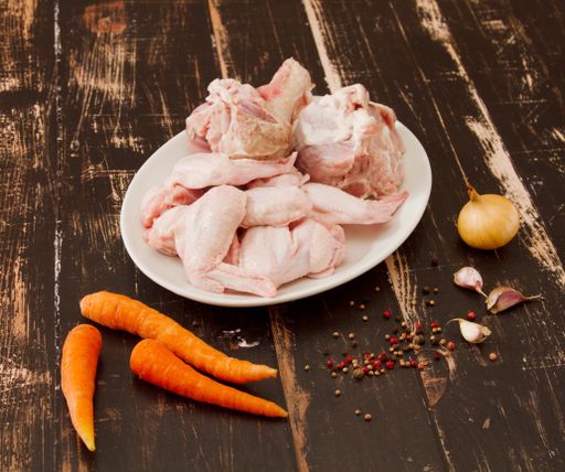 A wooden table with a plate of raw chicken pieces and vegetables
