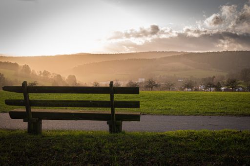 A bench near the pathway in the middle of a grassy field with mountains in the distance