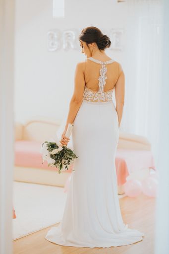 A vertical shot of a back of the bride wearing a bridal dress and holding a bouquet