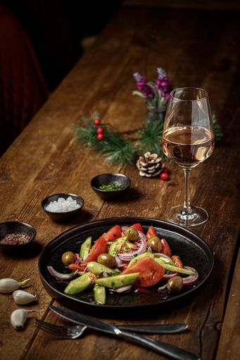 A vertical shot of a fresh salad with a glass of wine and Christmas decorations on a wooden table