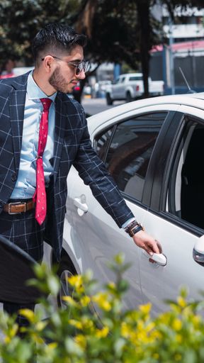 A handsome male in elegant checkered suit and sunglasses opening the car door