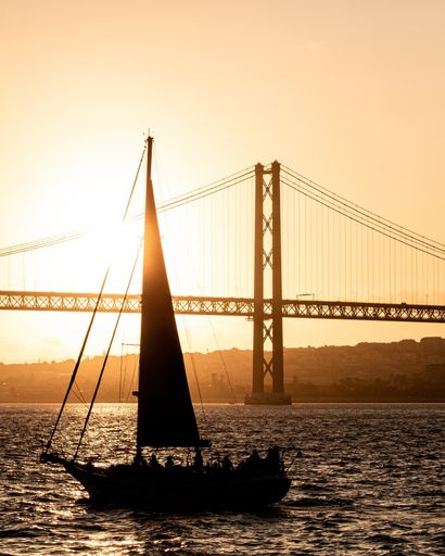 A vertical low angle shot of the 25 of April bridge during sunset with a silhouetted boat in the foreground