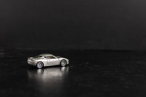 A selective focus shot of a silver toy sports car on a black surface