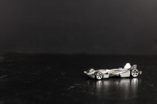 A selective focus shot of a silver toy sports car on a black surface