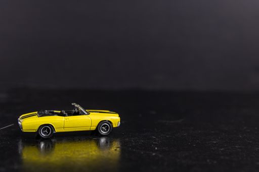 A selective focus shot of a yellow toy car with black stripes on a black surface