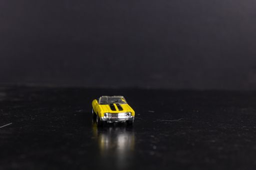 A selective focus shot of a yellow toy car with black stripes on a black surface
