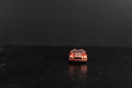 A selective focus shot of an orange toy car with silver stripes on a black surface