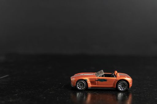 A selective focus shot of an orange toy car with silver stripes on a black surface