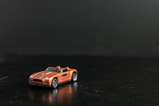 A selective focus shot of an orange toy car with silver stripes on a black surface