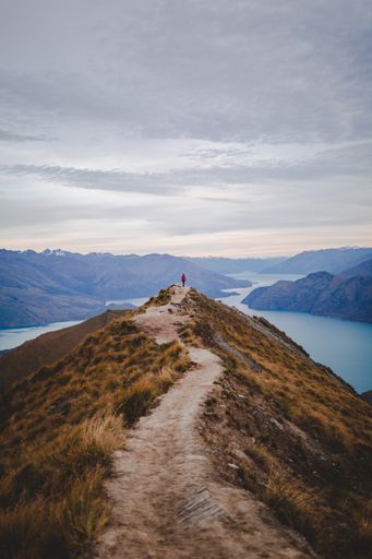 A vertical high angle shot of a person standing on the end of a walking road on Roys Peak in New Zealand under a beautiful cloudy sky