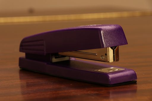A closeup shot of a purple stapler on a wooden surface