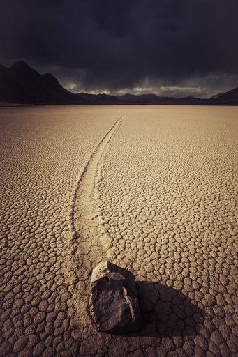 A vertical shot of a deserted ground of sand surrounded by a mountainous scenery