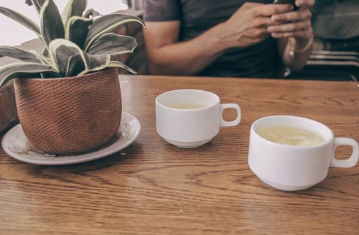 A shot of two cups of lemon tea on a wooden table with a decorative pot with a green plant in a cafe