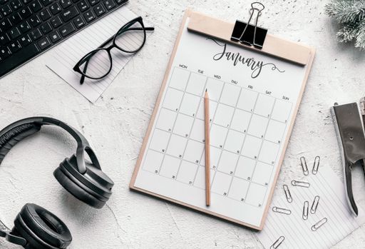 The flat lay of a calendar diary, glasses, clips, stapler, headphones, keyboard, and pencil - motivation for a fresh start