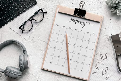 The flat lay of business planning concept - a calendar diary, glasses, clips, stapler, headphones, keyboard, and pencil