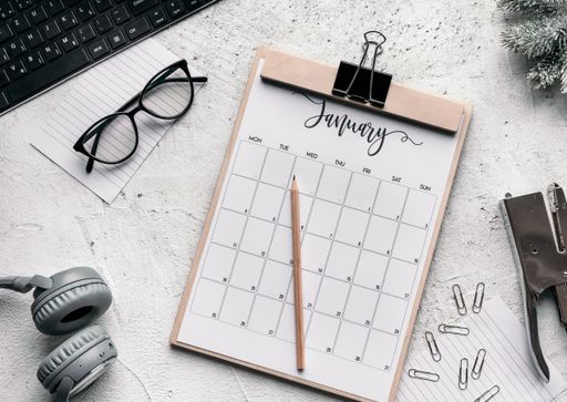 The flat lay of motivation and planning concept - a calendar diary, glasses, clips, stapler, headphones, keyboard, and pencil