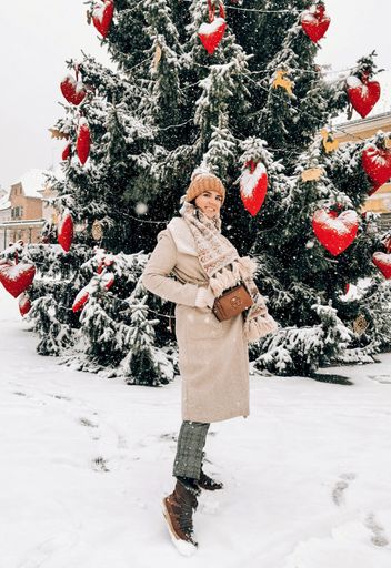 A pretty young female posing in the background of an outdoor Christmas tree decorated with heart-shaped toys