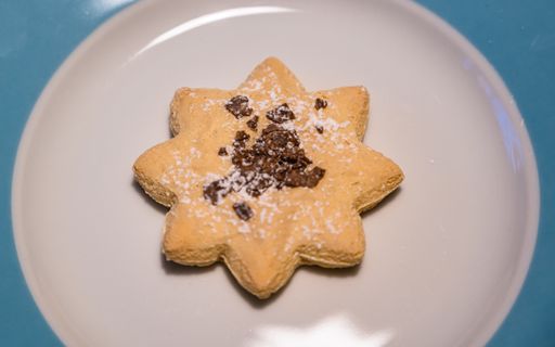 A selective focus shot of a star-shaped cookie with chocolate and powdered sugar on a white plate
