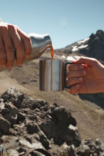Two hands pouring a liquid into a mug resting with a beautiful mountain landscape in the background