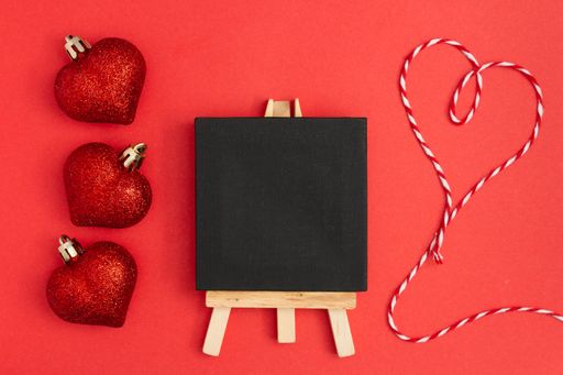 A top view of red heart shape balls, a blackboard, and heart thread on a red background
