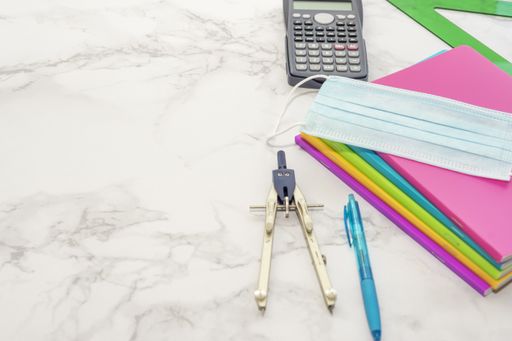 A closeup shot of notebooks, protective mask, pens, calculator, ruler, compass on marble background