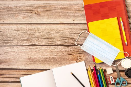A sanitary mask, colored pencils, notebooks, scissors, sharpener, rubber on a wooden table