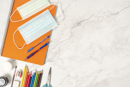 A closeup of sanitary masks, pens, pencils, notebooks, scissors, sharpener, rubber on a marble table