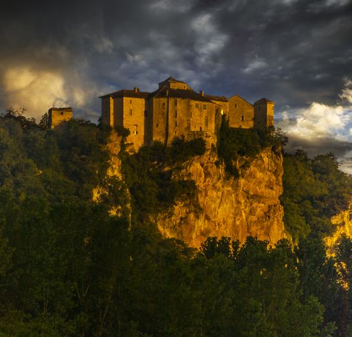 The Chateau de Bruniquel surrounded by greenery and rocks under a cloudy sky during sunset in France