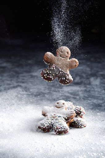Two gingerbread man cookies with happy faces in snowy Christmas scene. Falling snow