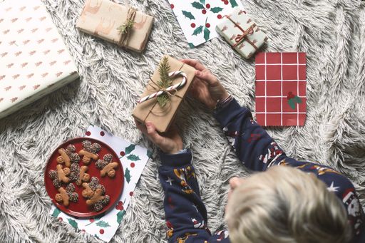 A child lying on the rug holds a gift wrapped in recycled paper and a candy stick