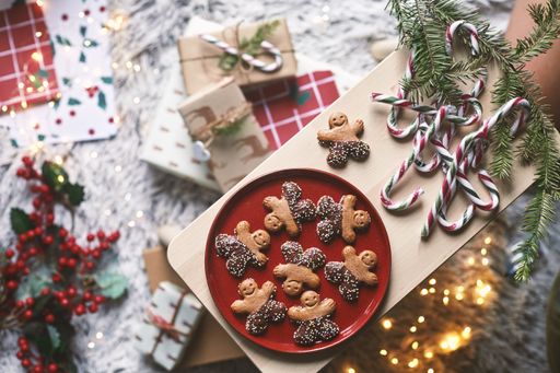 A top view of gingerbread cookies on a red plate on a wooden board with candy sticks