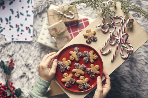 A top view of hands putting a red plate with gingerbread cookies on a wooden board with candy sticks