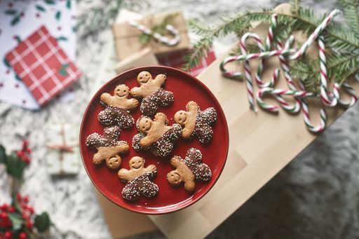 A top view of gingerbread cookies on a red plate on a wooden board with candy sticks