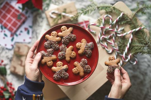 A top view of hands putting a gingerbread cookie on a red plate on a wooden board with candy sticks