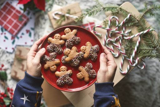 A top view of hands putting a red plate with gingerbread cookies on a wooden board with candy sticks