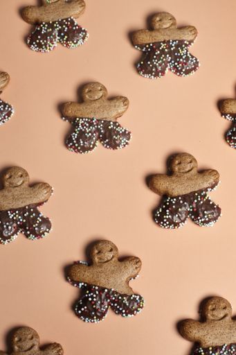 A top view of gingerbread man cookies with chocolate and anise balls on a light brown backgroun