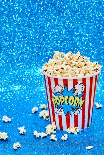 A vertical shot of a big paper cup filled with popcorn on a shiny blue surface