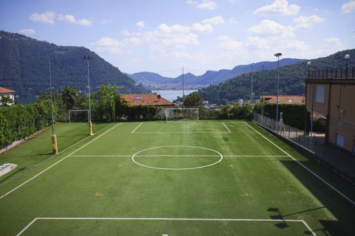 A green football pitch on the background of the mountains under the cloudy sky on a sunny day