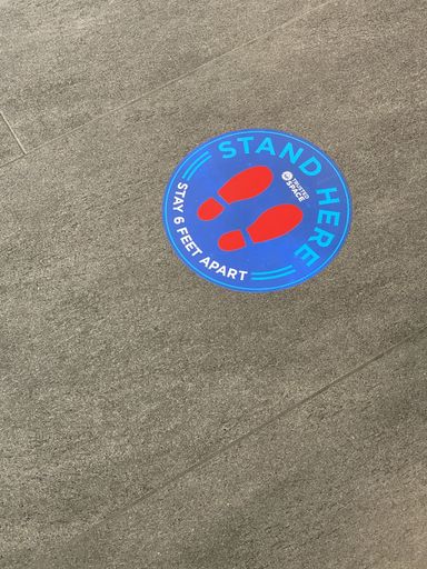 A vertical shot of a circle symbol sign printed on the ground with a warning to stay 6 feet apart