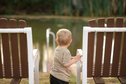 A shallow focus shot of a cute blonde kid near chairs by the lake