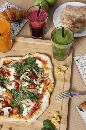 A vertical shot of an artisan pizza on the wooden board with smoothies and pastries.