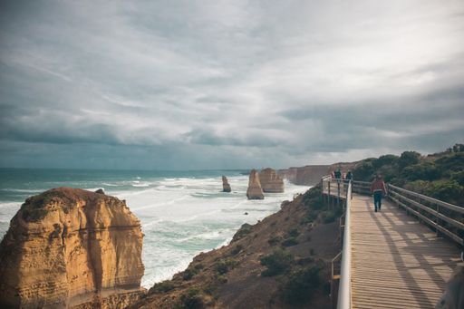 A group of people walking on a boardwalk near the sea with a lot of rock formations