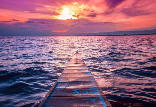 A beautiful shot of the nose of a small boat sailing in the sea with amazing breathtaking clouds in the red sky during sunset