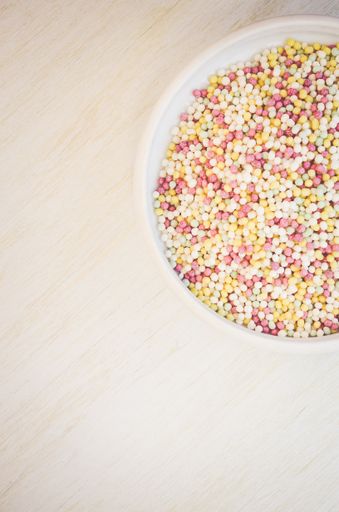 A vertical top view of small colored balls on a bowl in a wooden table
