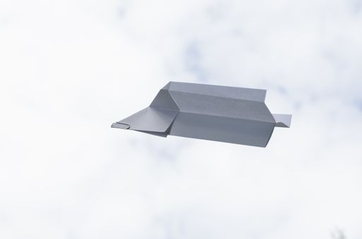 A closeup shot of a paper airplane with paper clip against a sky