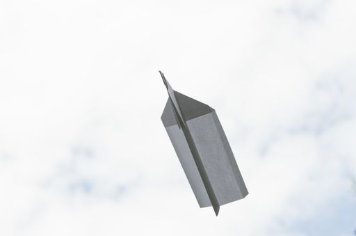 A low angle shot of a paper airplane with paper clip against a sky
