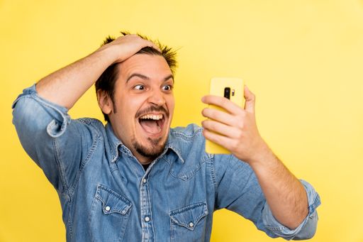 A young Caucasian male showing excitement after seeing something on the phone against a yellow background